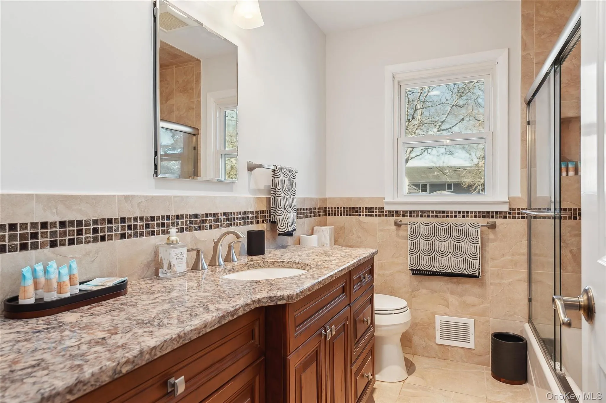 Bathroom featuring vanity, tile walls, tile patterned floors, and toilet Bathroom featuring vanity, tile walls, tile patterned floors, and toilet