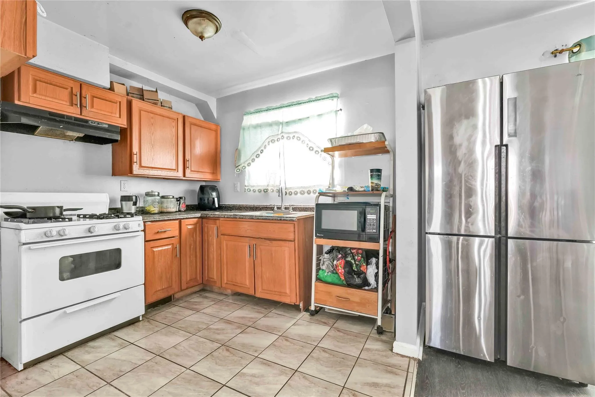 Kitchen featuring light tile patterned flooring, sink, stainless steel refrigerator, and white gas range oven Kitchen featuring light tile patterned flooring, sink, stainless steel refrigerator, and white gas range oven