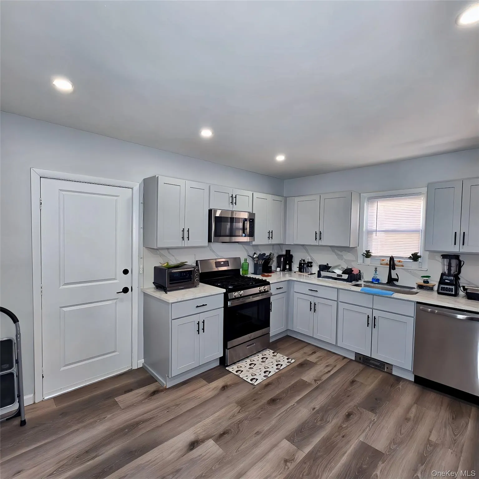 Kitchen with dark wood-style floors, stainless steel appliances, a sink, and light countertops Kitchen with dark wood-style floors, stainless steel appliances, a sink, and light countertops