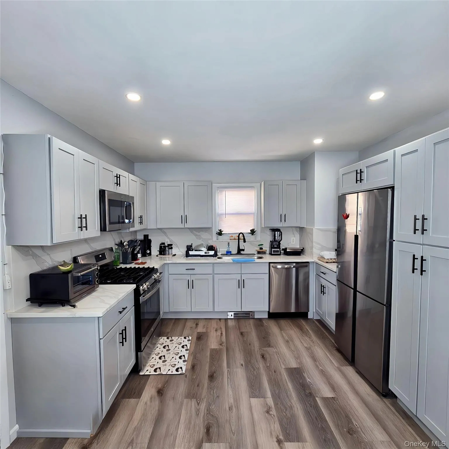 Kitchen featuring tasteful backsplash, dark wood-style flooring, stainless steel appliances, light countertops, and a sink Kitchen featuring tasteful backsplash, dark wood-style flooring, stainless steel appliances, light countertops, and a sink