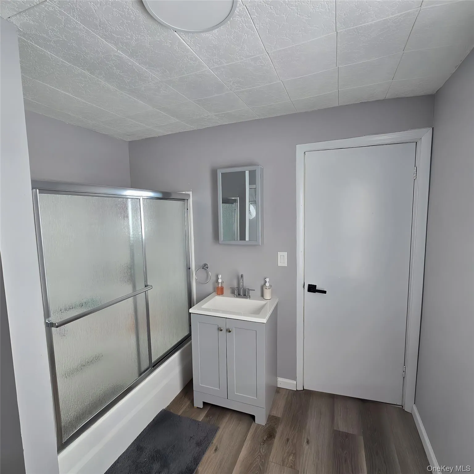 Bathroom featuring baseboards, combined bath / shower with glass door, wood finished floors, and vanity Bathroom featuring baseboards, combined bath / shower with glass door, wood finished floors, and vanity