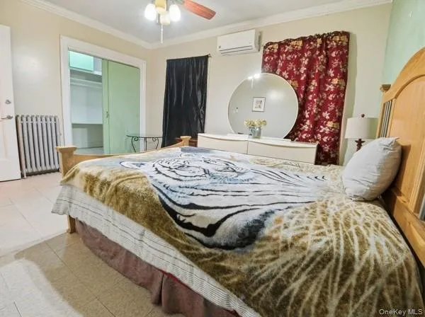 Tiled bedroom with crown molding, radiator heating unit, a closet, a wall mounted AC, and ceiling fan Tiled bedroom with crown molding, radiator heating unit, a closet, a wall mounted AC, and ceiling fan