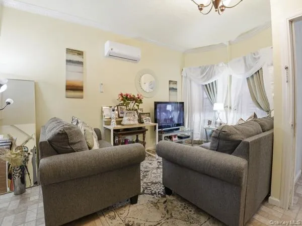 Living room with a chandelier, ornamental molding, and a wall mounted AC Living room with a chandelier, ornamental molding, and a wall mounted AC