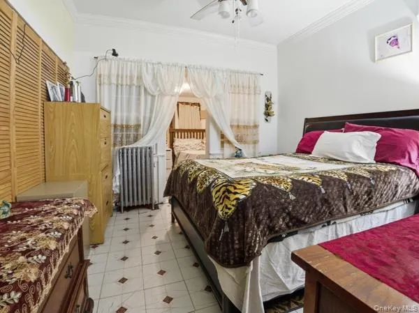 Bedroom with a closet, radiator heating unit, ornamental molding, and ceiling fan Bedroom with a closet, radiator heating unit, ornamental molding, and ceiling fan
