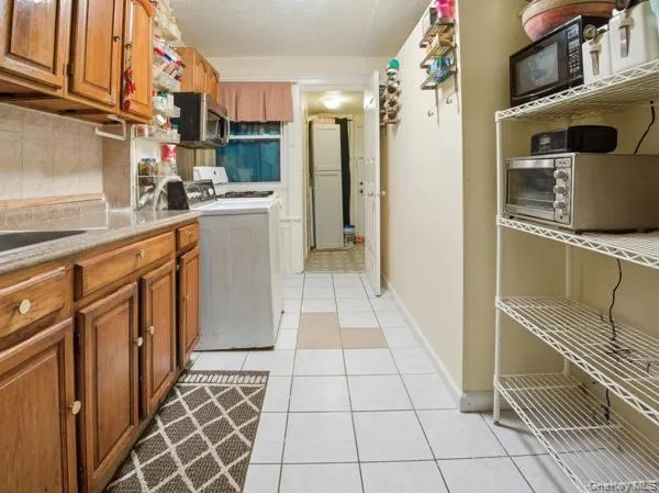 Kitchen with washer / dryer, black microwave, brown cabinets, stainless steel microwave, and a textured ceiling Kitchen with washer / dryer, black microwave, brown cabinets, stainless steel microwave, and a textured ceiling