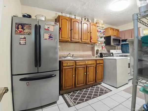 Kitchen with appliances with stainless steel finishes, washer / clothes dryer, brown cabinetry, light countertops, and a textured ceiling Kitchen with appliances with stainless steel finishes, washer / clothes dryer, brown cabinetry, light countertops, and a textured ceiling