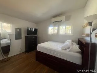 Bedroom featuring a wall unit AC, dark wood finished floors, lofted ceiling, electric panel, and baseboards Bedroom featuring a wall unit AC, dark wood finished floors, lofted ceiling, electric panel, and baseboards