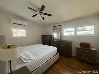 Bedroom featuring lofted ceiling, a ceiling fan, dark wood-style flooring, and a wall mounted AC Bedroom featuring lofted ceiling, a ceiling fan, dark wood-style flooring, and a wall mounted AC