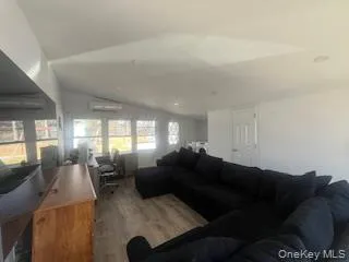 Living area with lofted ceiling, a wall mounted air conditioner, and light wood-style floors Living area with lofted ceiling, a wall mounted air conditioner, and light wood-style floors
