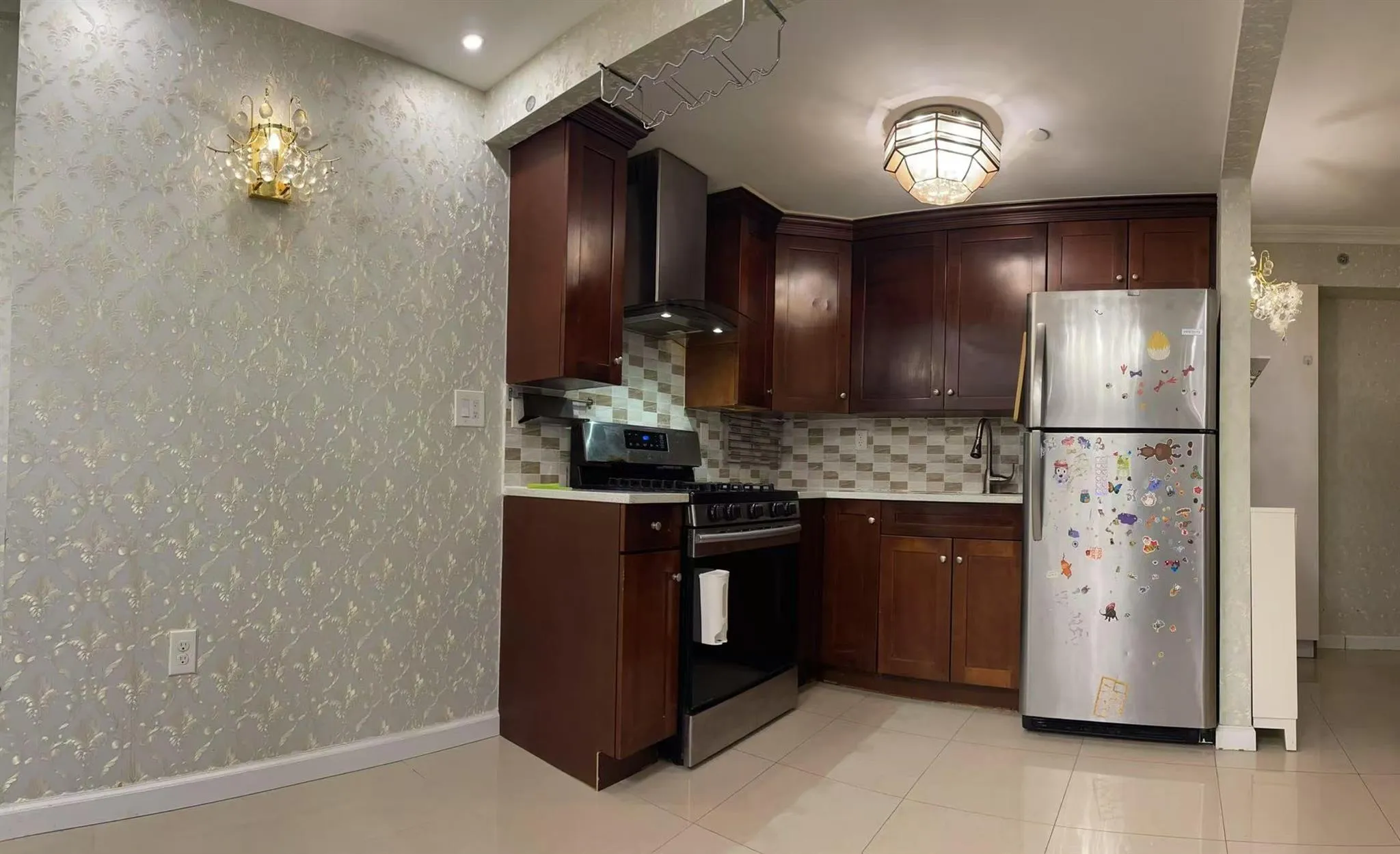 Kitchen featuring wall chimney range hood, sink, light tile patterned floors, appliances with stainless steel finishes, and backsplash Kitchen featuring wall chimney range hood, sink, light tile patterned floors, appliances with stainless steel finishes, and backsplash