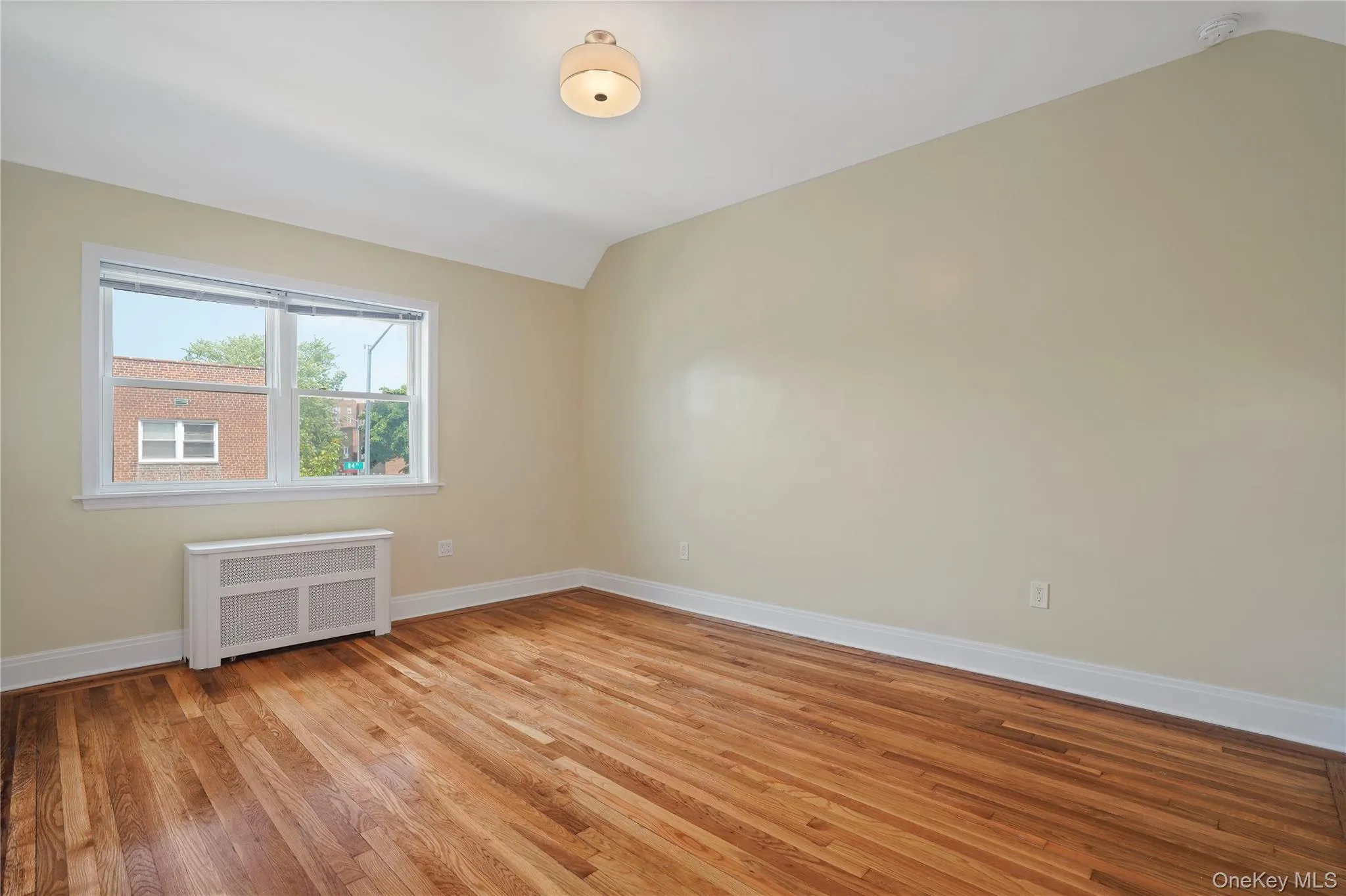 Spare room featuring radiator heating unit, vaulted ceiling, a smoke detector, and light wood-type flooring Spare room featuring radiator heating unit, vaulted ceiling, a smoke detector, and light wood-type flooring