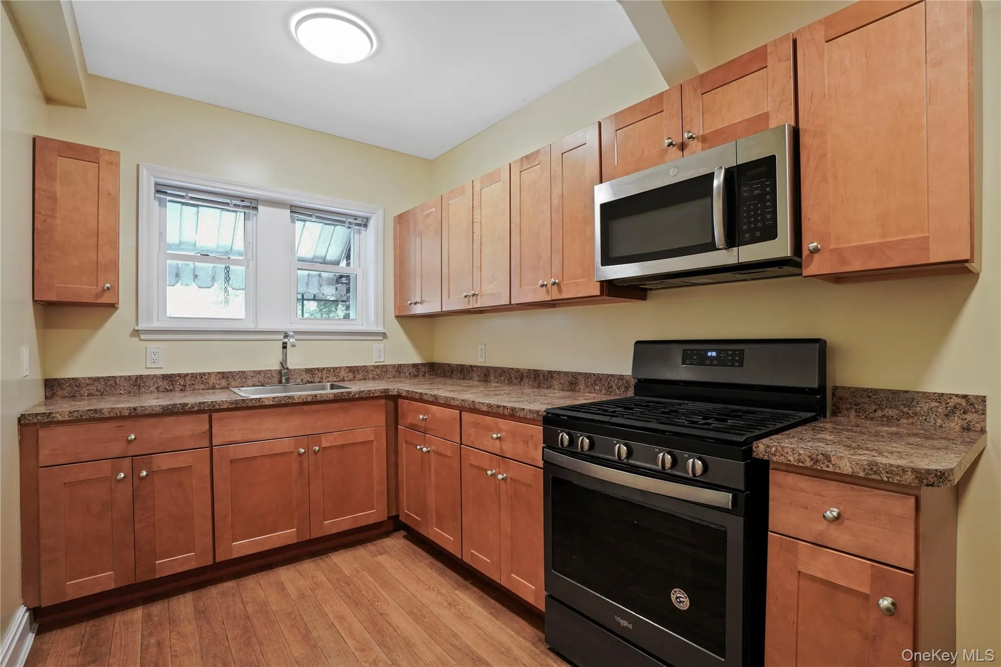 Kitchen with stainless steel appliances, dark countertops, light wood finished floors, and brown cabinetry Kitchen with stainless steel appliances, dark countertops, light wood finished floors, and brown cabinetry