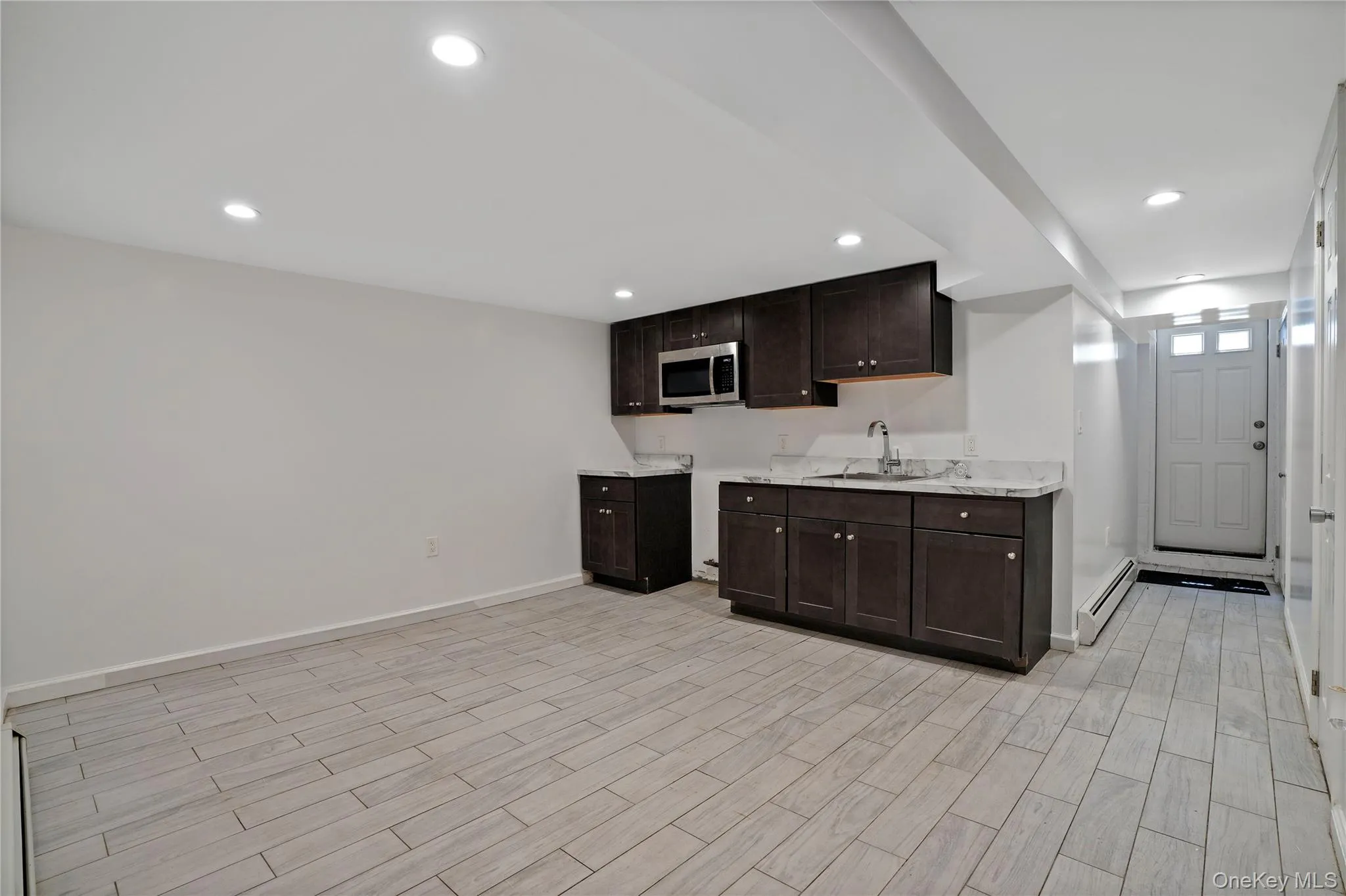 Kitchen with stainless steel microwave, a baseboard heating unit, dark brown cabinets, light wood-style flooring, and recessed lighting Kitchen with stainless steel microwave, a baseboard heating unit, dark brown cabinets, light wood-style flooring, and recessed lighting