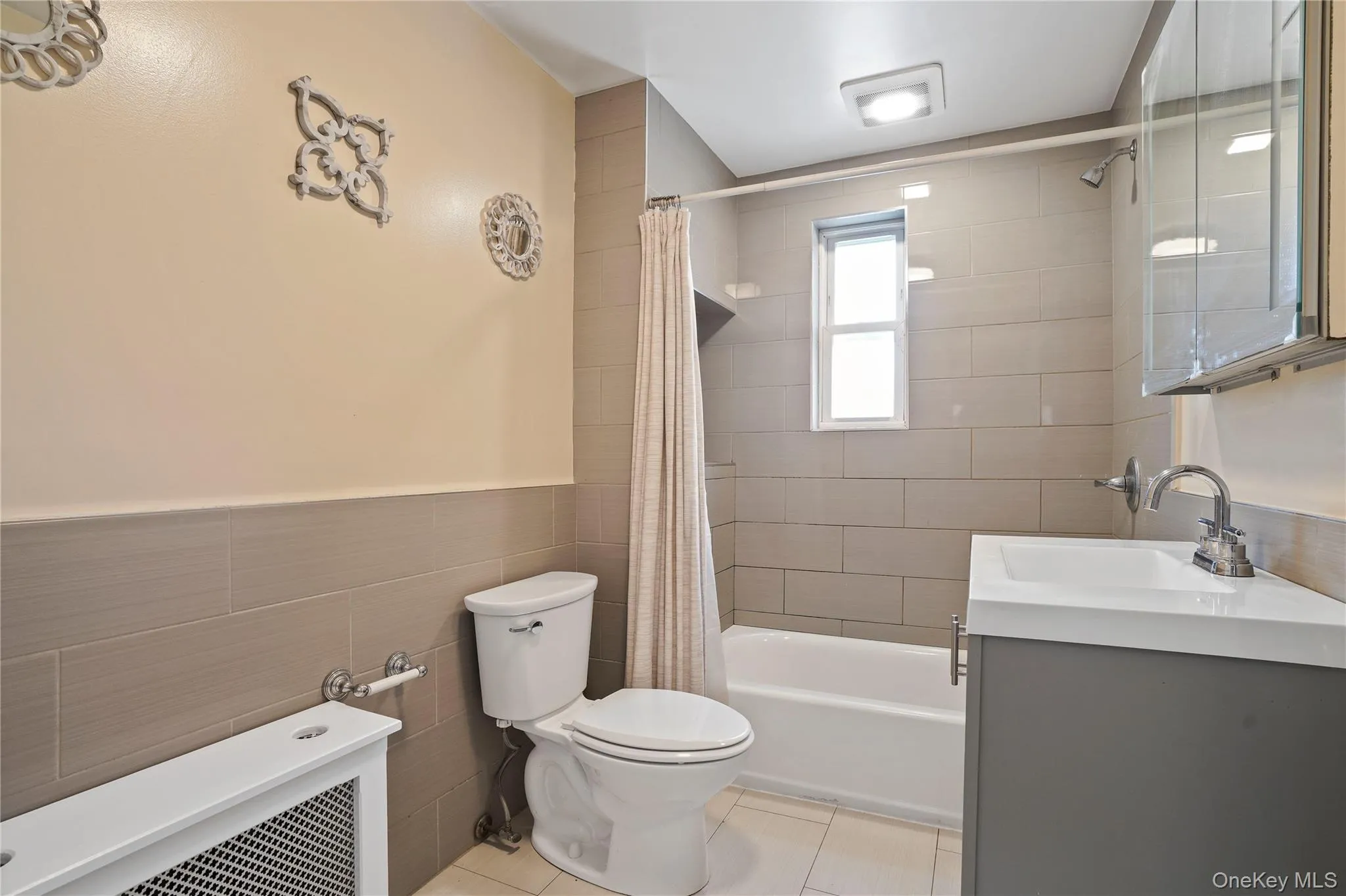 Full bathroom with tile walls, shower / bathtub combination with curtain, vanity, tile patterned floors, and wainscoting Full bathroom with tile walls, shower / bathtub combination with curtain, vanity, tile patterned floors, and wainscoting