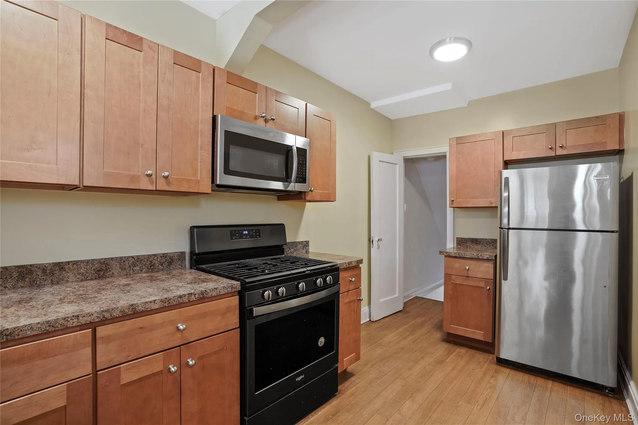 Kitchen with stainless steel appliances, light wood-type flooring, and dark countertops Kitchen with stainless steel appliances, light wood-type flooring, and dark countertops