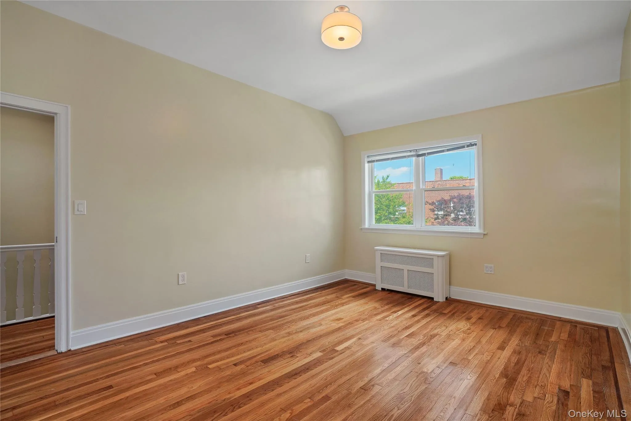 Unfurnished room with radiator, light wood-type flooring, and lofted ceiling Unfurnished room with radiator, light wood-type flooring, and lofted ceiling