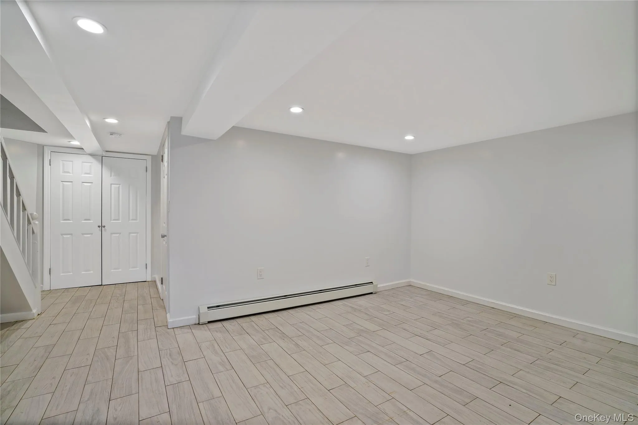 Finished below grade area featuring a baseboard heating unit, recessed lighting, light wood finished floors, and stairway Finished below grade area featuring a baseboard heating unit, recessed lighting, light wood finished floors, and stairway