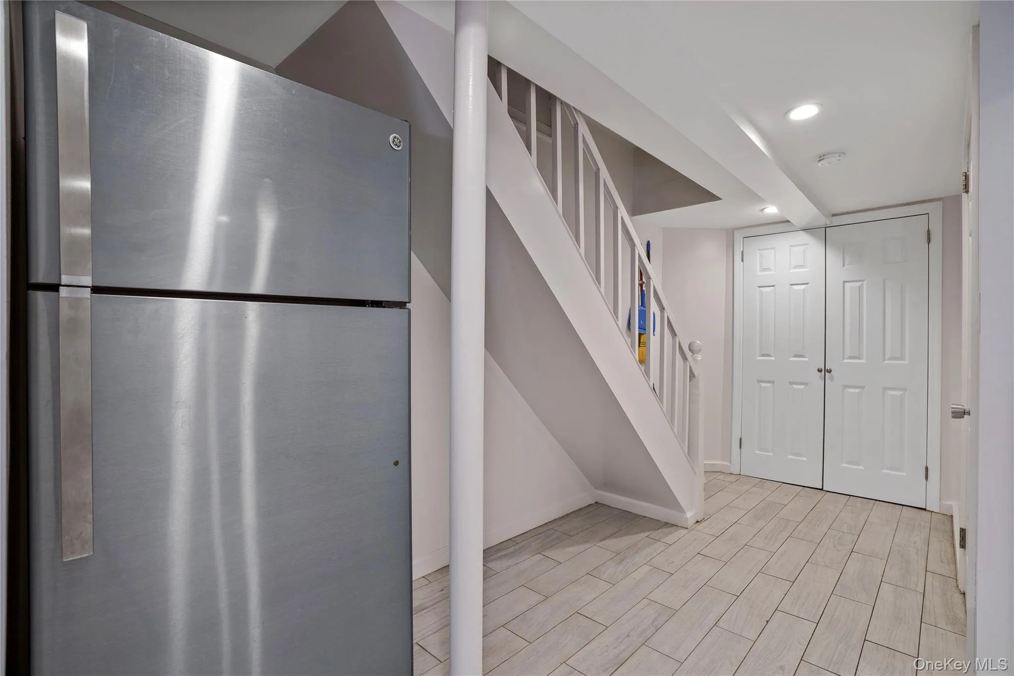 Finished below grade area featuring freestanding refrigerator, wood finished floors, stairway, and recessed lighting Finished below grade area featuring freestanding refrigerator, wood finished floors, stairway, and recessed lighting