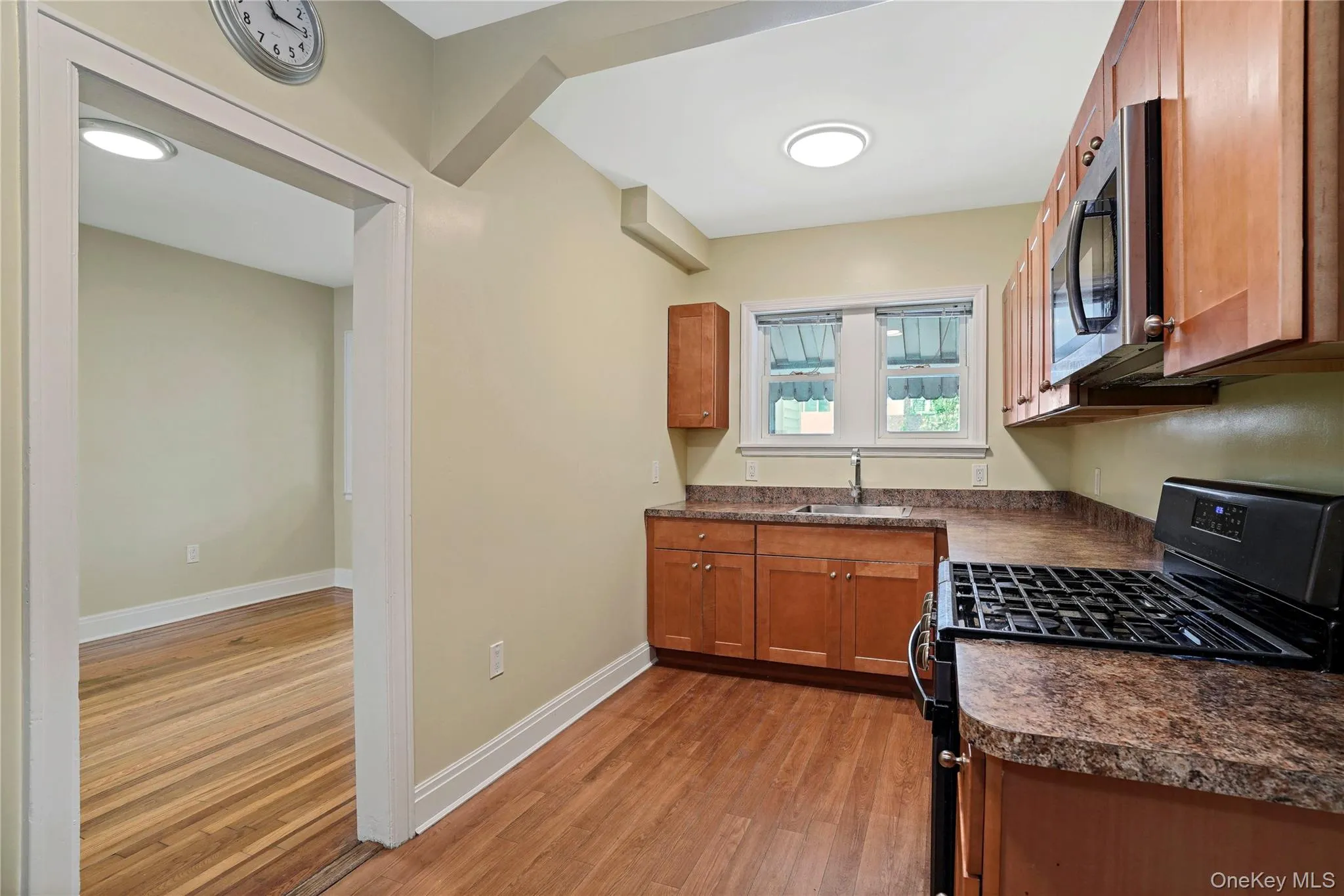 Kitchen with black gas range oven, stainless steel microwave, dark countertops, light wood finished floors, and brown cabinetry Kitchen with black gas range oven, stainless steel microwave, dark countertops, light wood finished floors, and brown cabinetry
