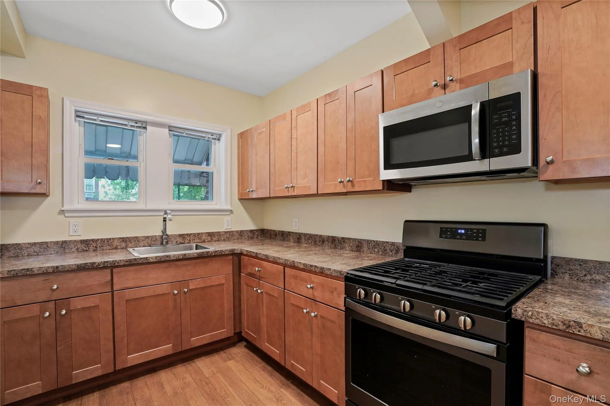 Kitchen featuring appliances with stainless steel finishes, dark countertops, light wood-type flooring, and brown cabinets Kitchen featuring appliances with stainless steel finishes, dark countertops, light wood-type flooring, and brown cabinets
