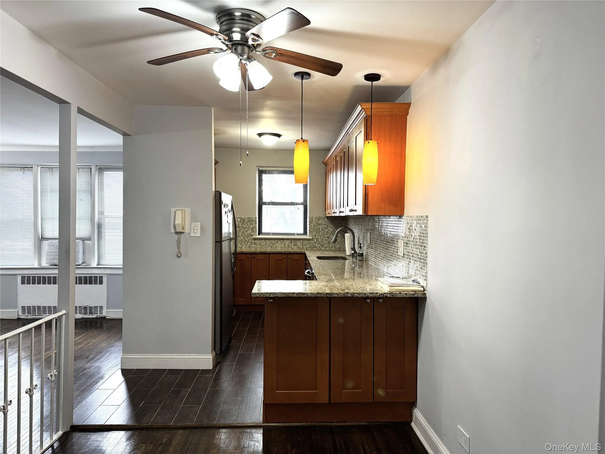 Kitchen with sink, radiator heating unit, stainless steel fridge, light stone countertops, and decorative backsplash Kitchen with sink, radiator heating unit, stainless steel fridge, light stone countertops, and decorative backsplash