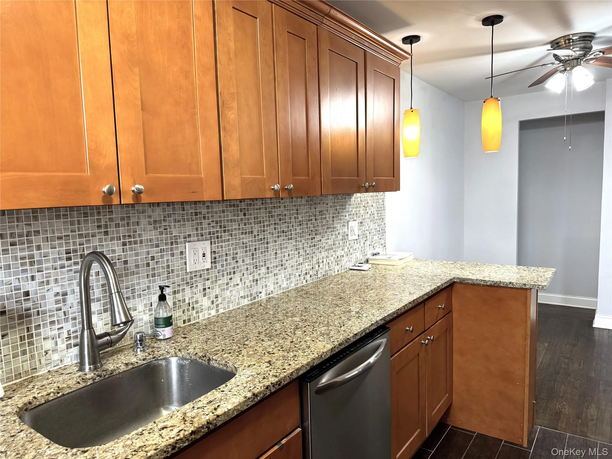 Kitchen with sink, dishwasher, hanging light fixtures, dark hardwood / wood-style floors, and light stone counters Kitchen with sink, dishwasher, hanging light fixtures, dark hardwood / wood-style floors, and light stone counters