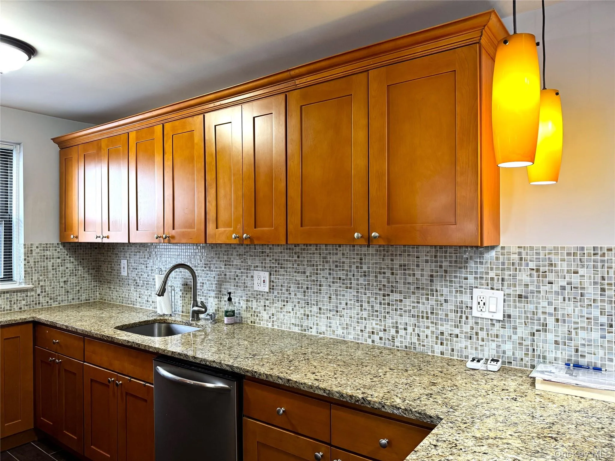 Kitchen with dishwasher, sink, light stone counters, and decorative light fixtures Kitchen with dishwasher, sink, light stone counters, and decorative light fixtures