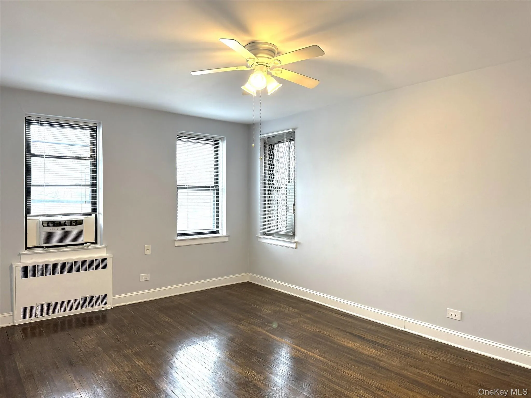 Spare room with cooling unit, dark hardwood / wood-style flooring, radiator heating unit, and ceiling fan Spare room with cooling unit, dark hardwood / wood-style flooring, radiator heating unit, and ceiling fan