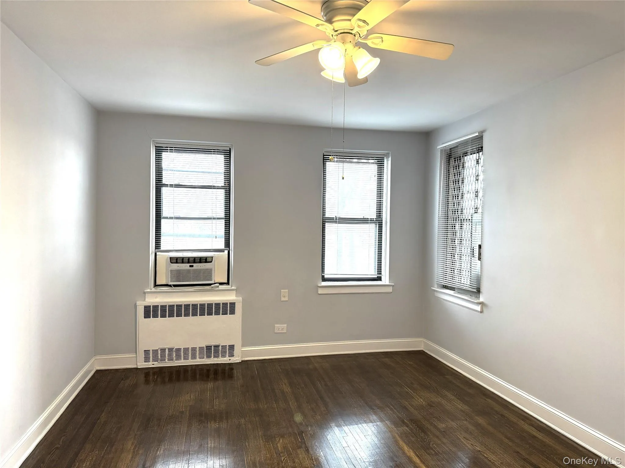 Empty room featuring a healthy amount of sunlight, radiator, cooling unit, and dark wood-type flooring Empty room featuring a healthy amount of sunlight, radiator, cooling unit, and dark wood-type flooring