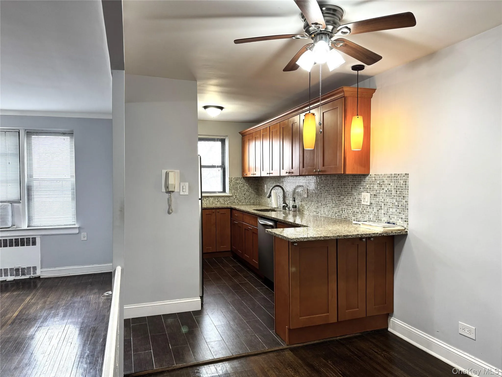 Kitchen with radiator, dishwasher, dark hardwood / wood-style flooring, decorative backsplash, and light stone countertops Kitchen with radiator, dishwasher, dark hardwood / wood-style flooring, decorative backsplash, and light stone countertops