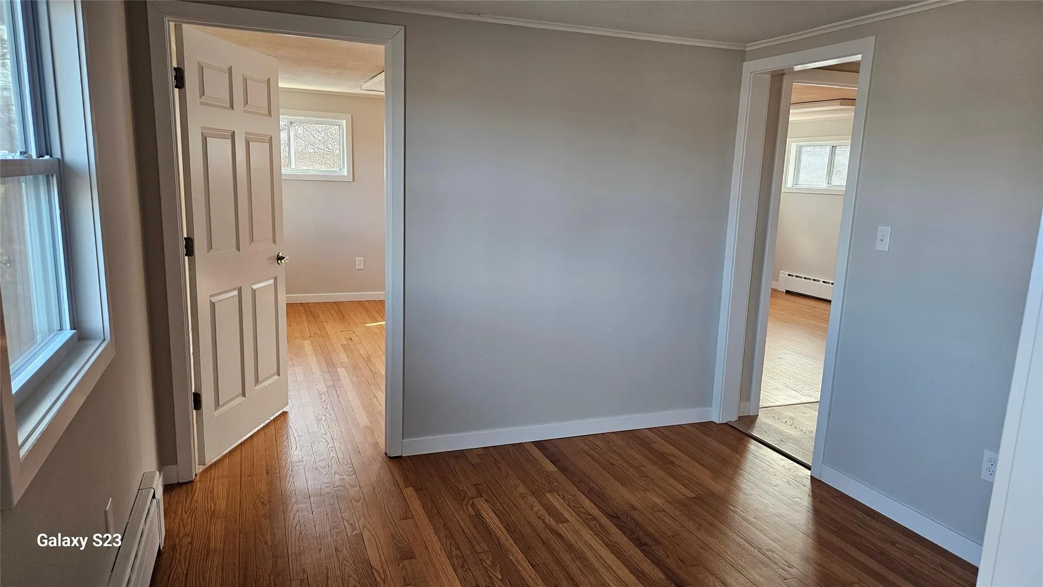 Hall featuring a baseboard radiator, wood-type flooring, crown molding, and a healthy amount of sunlight Hall featuring a baseboard radiator, wood-type flooring, crown molding, and a healthy amount of sunlight