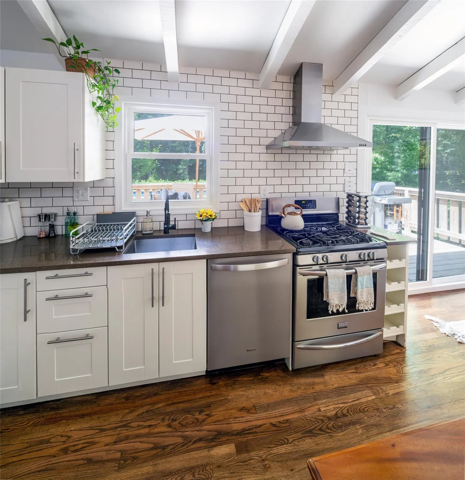 Kitchen with sink, appliances with stainless steel finishes, dark hardwood / wood-style flooring, wall chimney range hood, and white cabinets Kitchen with sink, appliances with stainless steel finishes, dark hardwood / wood-style flooring, wall chimney range hood, and white cabinets
