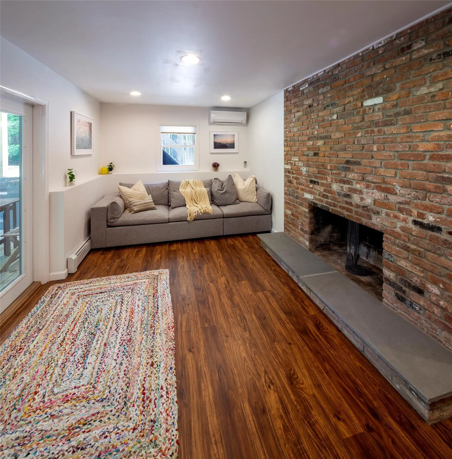 Unfurnished living room featuring a wealth of natural light, a brick fireplace, a baseboard heating unit, and a wall mounted air conditioner Unfurnished living room featuring a wealth of natural light, a brick fireplace, a baseboard heating unit, and a wall mounted air conditioner