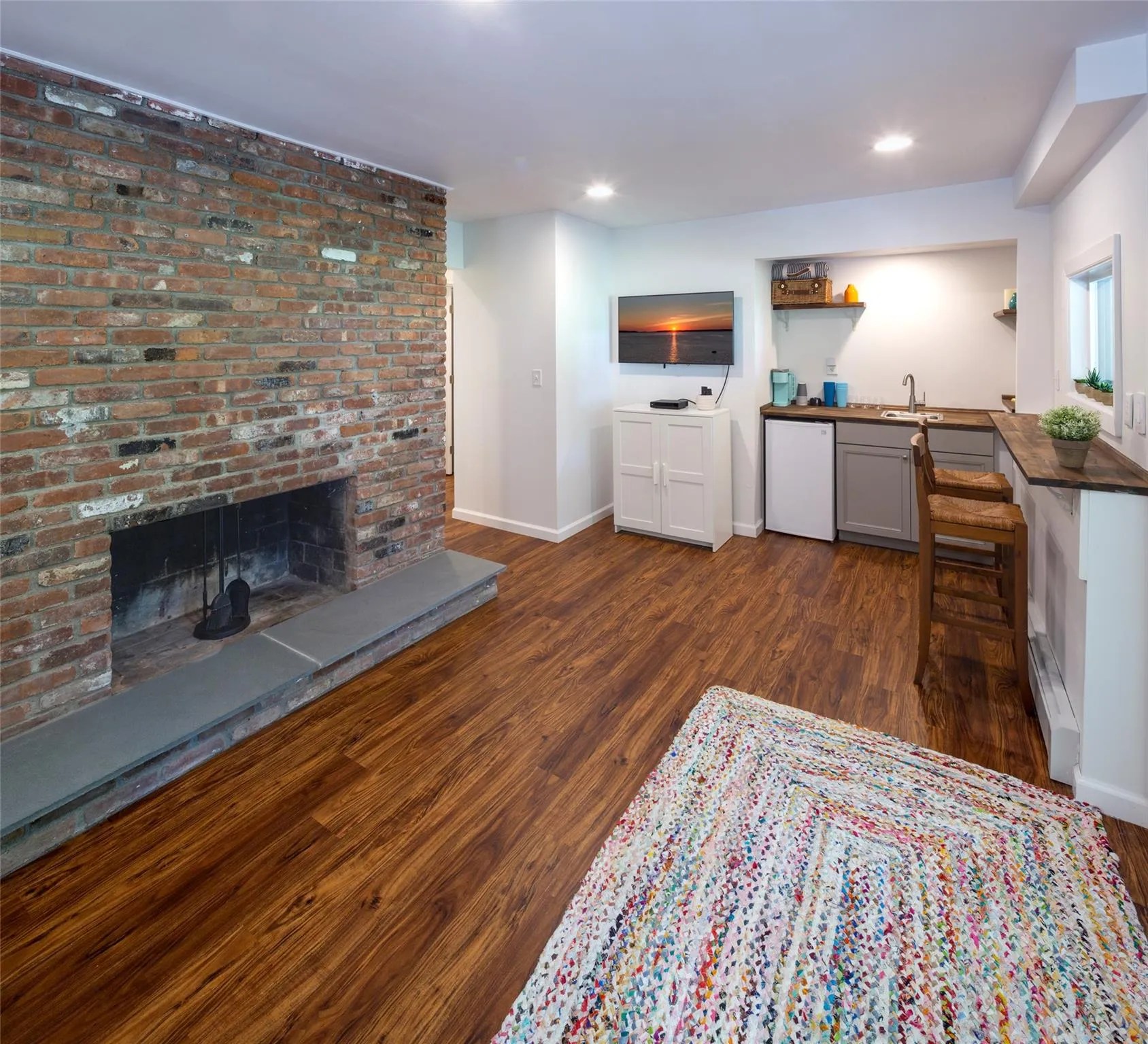 Living room featuring dark wood-type flooring, a fireplace, wet bar, and a baseboard heating unit Living room featuring dark wood-type flooring, a fireplace, wet bar, and a baseboard heating unit