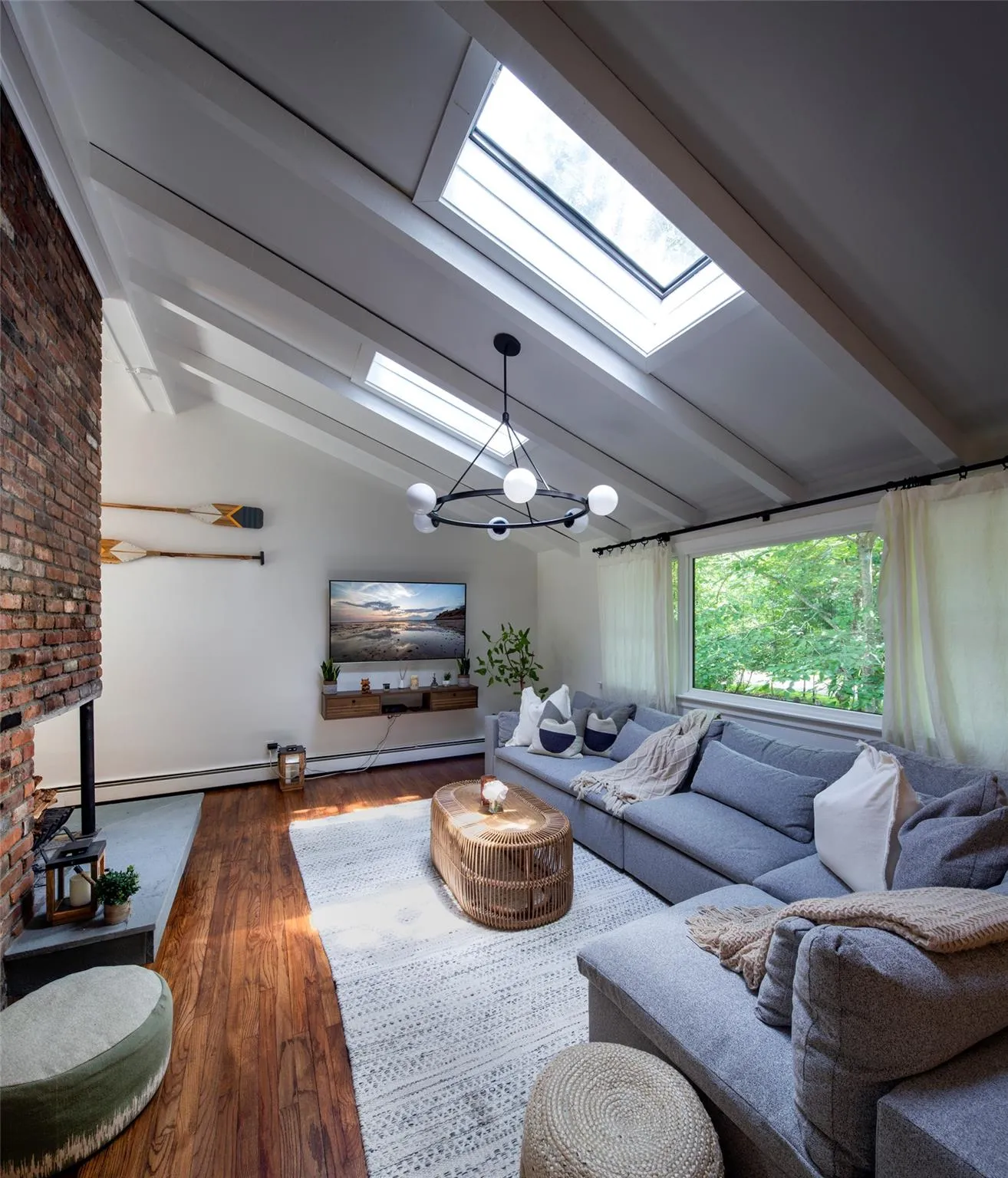 Living room with an inviting chandelier, dark hardwood / wood-style flooring, lofted ceiling with skylight, and baseboard heating Living room with an inviting chandelier, dark hardwood / wood-style flooring, lofted ceiling with skylight, and baseboard heating