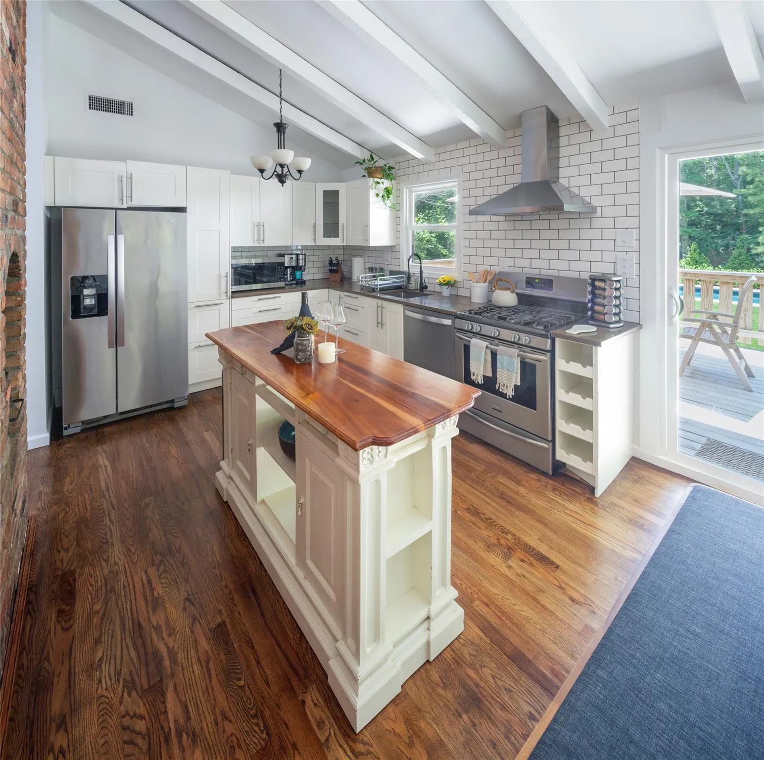 Kitchen with wall chimney range hood, wooden counters, hanging light fixtures, stainless steel appliances, and white cabinets Kitchen with wall chimney range hood, wooden counters, hanging light fixtures, stainless steel appliances, and white cabinets
