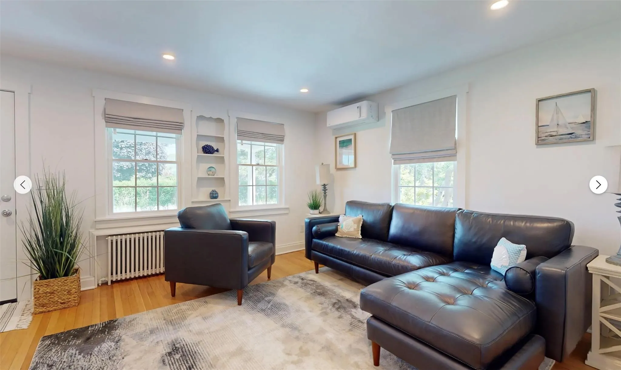 Living room featuring radiator heating unit, a wall mounted AC, and light wood-type flooring Living room featuring radiator heating unit, a wall mounted AC, and light wood-type flooring