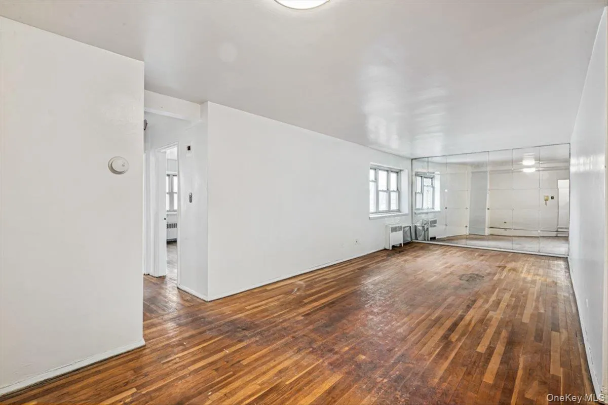 Unfurnished living room with radiator, hardwood / wood-style floors, and baseboard heating Unfurnished living room with radiator, hardwood / wood-style floors, and baseboard heating