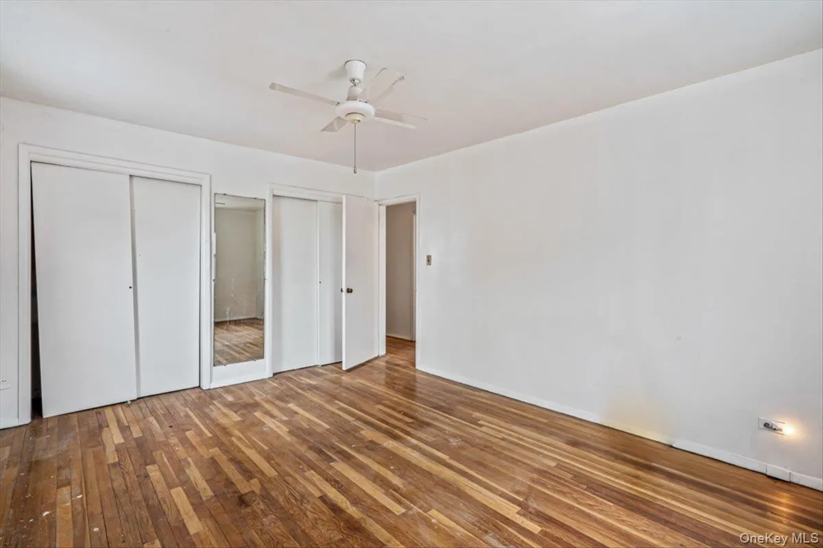 Unfurnished bedroom featuring multiple closets, hardwood / wood-style flooring, and ceiling fan Unfurnished bedroom featuring multiple closets, hardwood / wood-style flooring, and ceiling fan