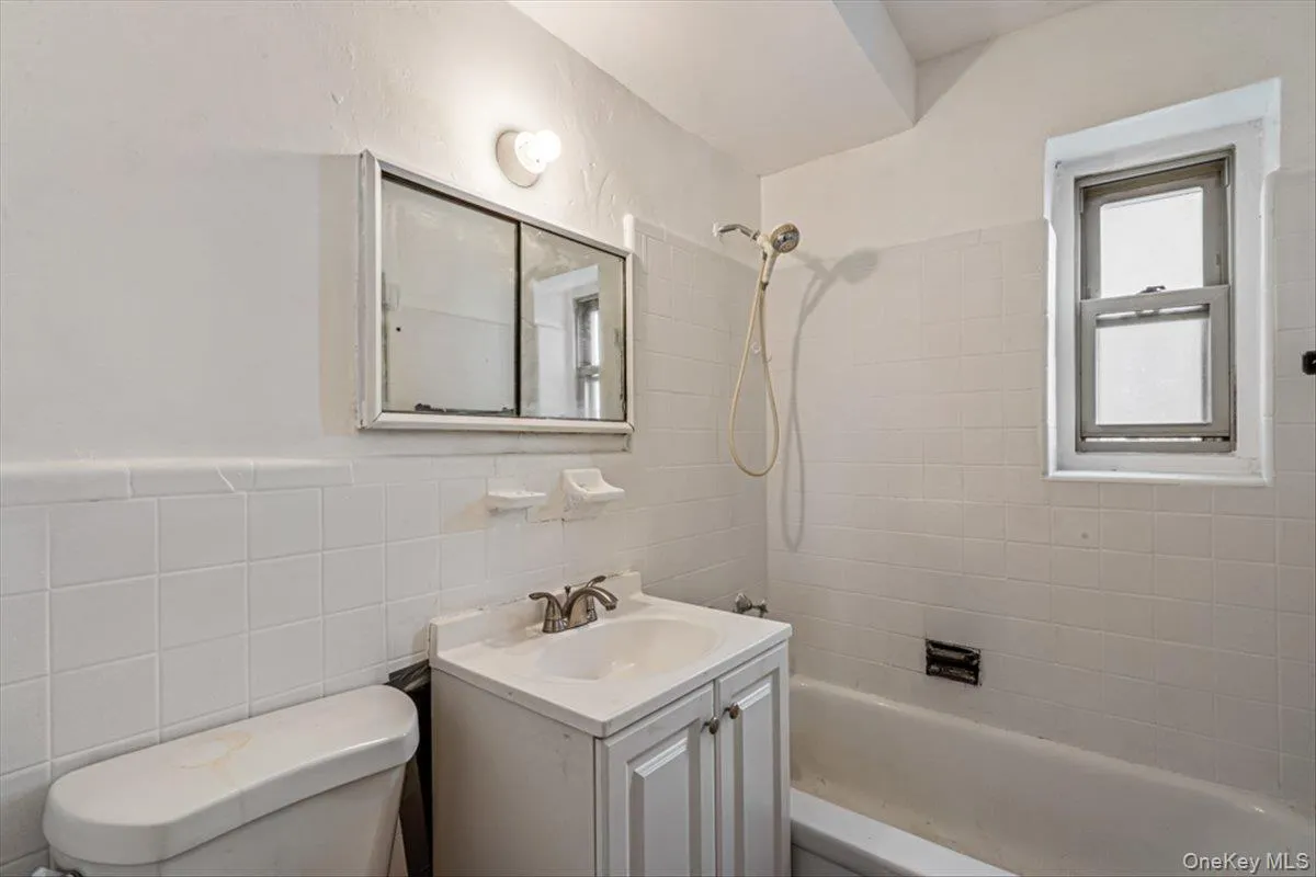 Full bathroom with vanity, tiled shower / bath combo, tile walls, and toilet Full bathroom with vanity, tiled shower / bath combo, tile walls, and toilet