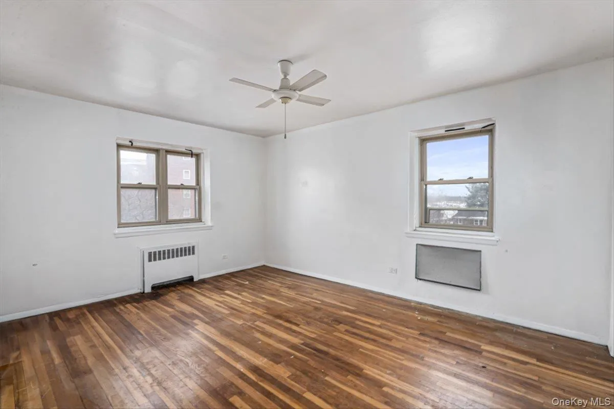 Unfurnished room with dark hardwood / wood-style floors, radiator heating unit, and ceiling fan Unfurnished room with dark hardwood / wood-style floors, radiator heating unit, and ceiling fan