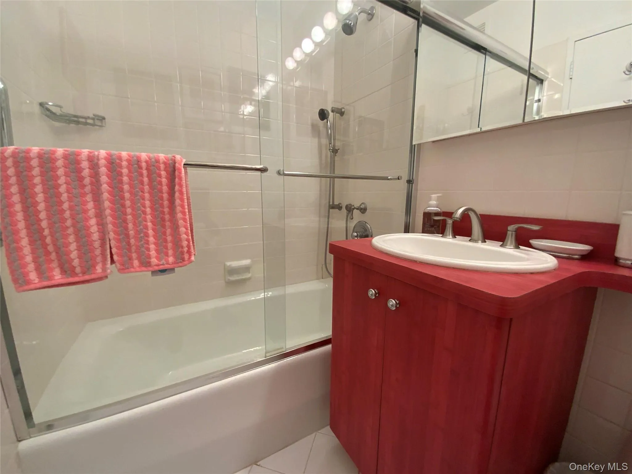 Bathroom with vanity, enclosed tub / shower combo, tasteful backsplash, light tile patterned floors, and tile walls Bathroom with vanity, enclosed tub / shower combo, tasteful backsplash, light tile patterned floors, and tile walls