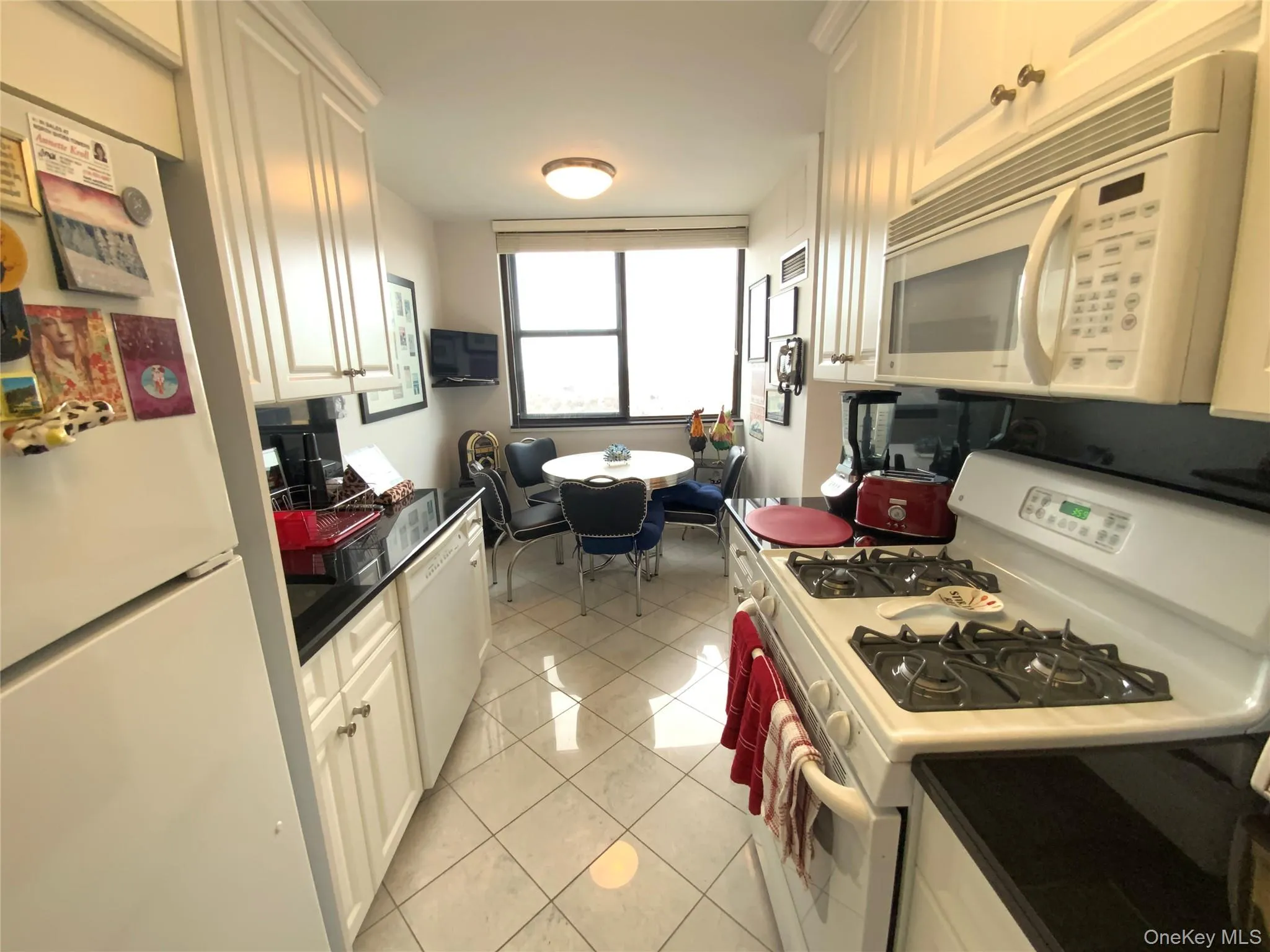 Kitchen featuring white appliances, dark countertops, white cabinetry, and light tile patterned floors Kitchen featuring white appliances, dark countertops, white cabinetry, and light tile patterned floors