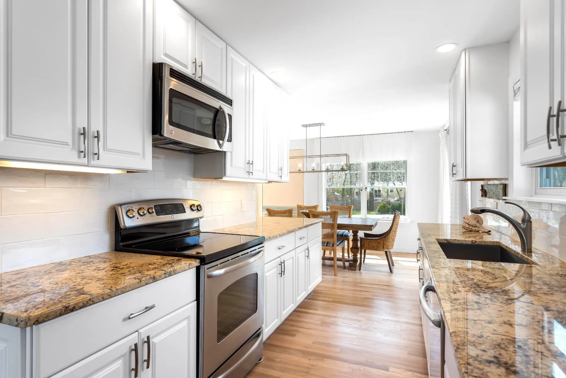 Kitchen featuring white cabinetry, sink, hanging light fixtures, and appliances with stainless steel finishes Kitchen featuring white cabinetry, sink, hanging light fixtures, and appliances with stainless steel finishes