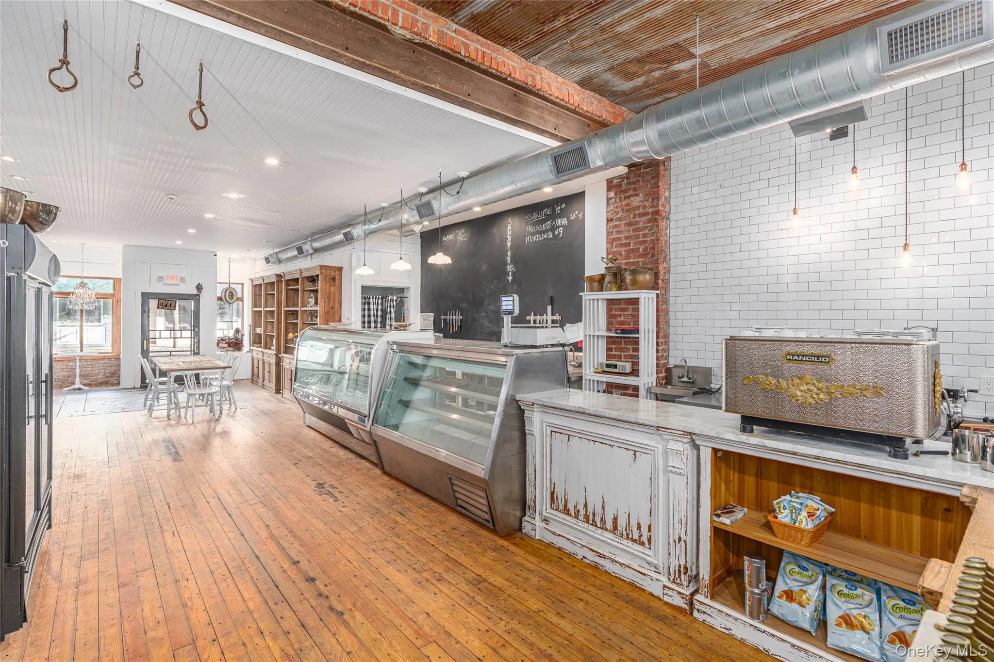 Kitchen featuring hanging light fixtures, beam ceiling, light stone counters, light hardwood / wood-style floors, and brick wall Kitchen featuring hanging light fixtures, beam ceiling, light stone counters, light hardwood / wood-style floors, and brick wall