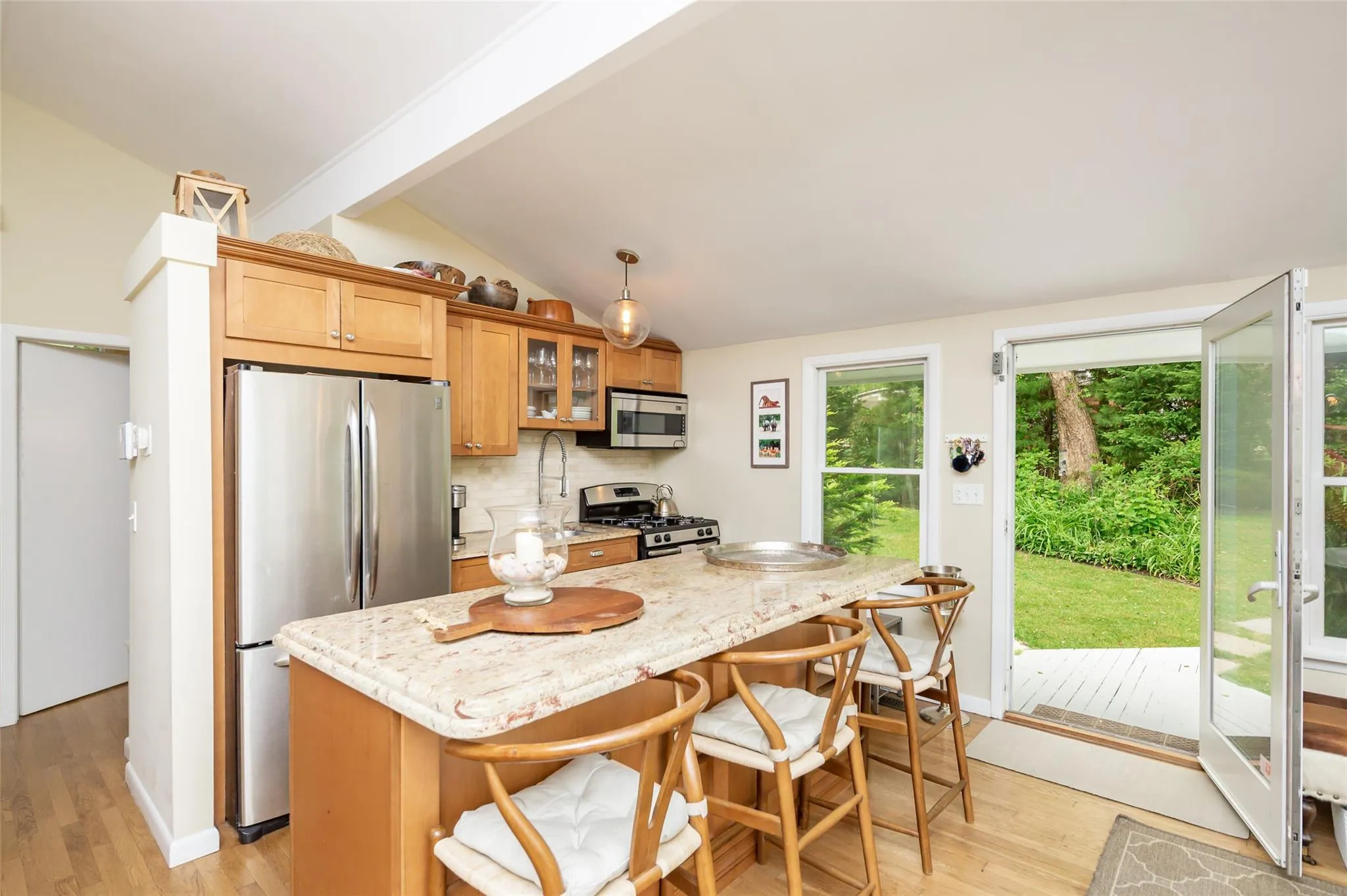 Kitchen featuring lofted ceiling with beams, tasteful backsplash, stainless steel appliances, and light wood-style flooring Kitchen featuring lofted ceiling with beams, tasteful backsplash, stainless steel appliances, and light wood-style flooring