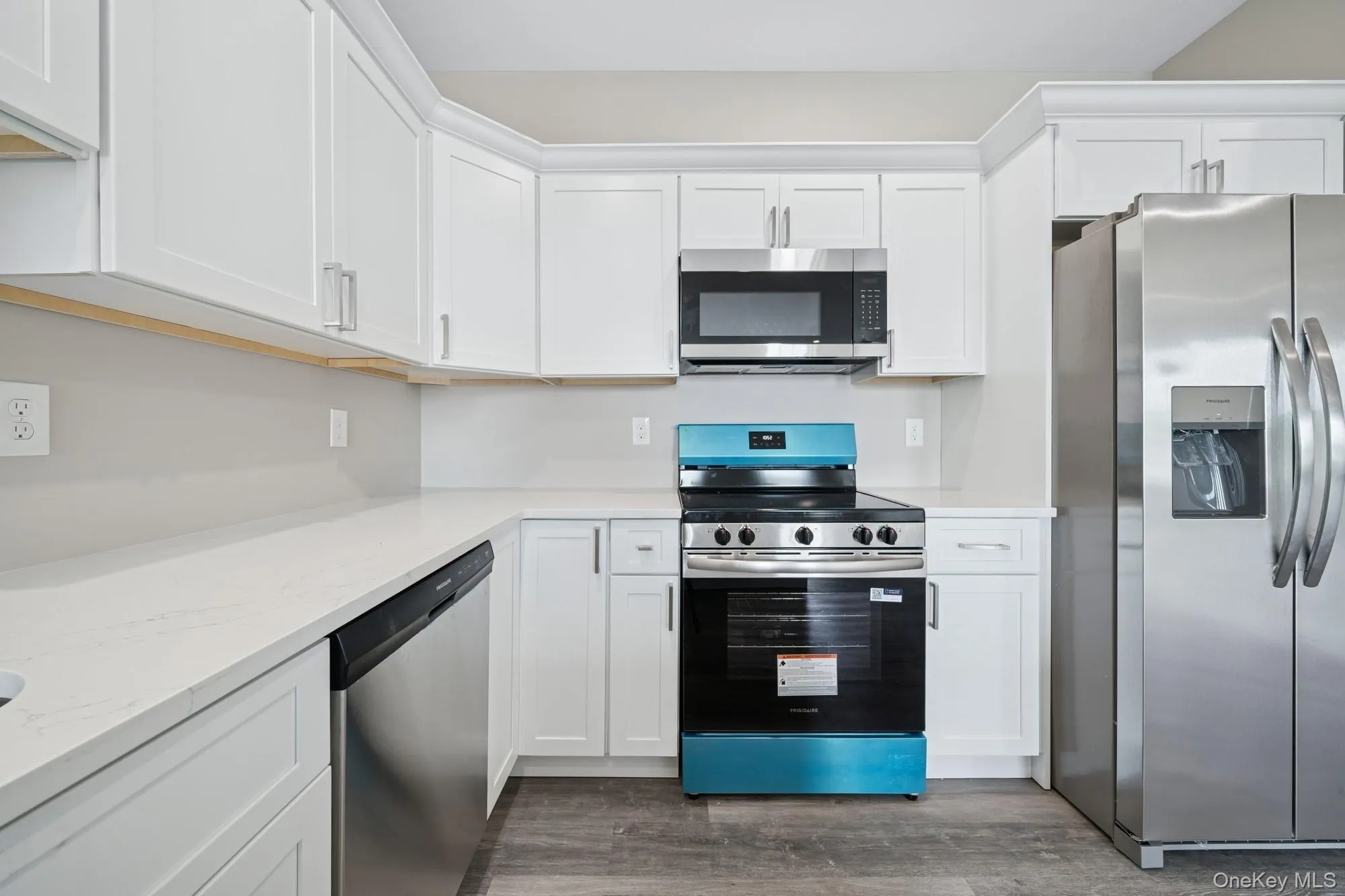 Kitchen with appliances with stainless steel finishes, dark wood-style flooring, white cabinetry, and light stone counters Kitchen with appliances with stainless steel finishes, dark wood-style flooring, white cabinetry, and light stone counters