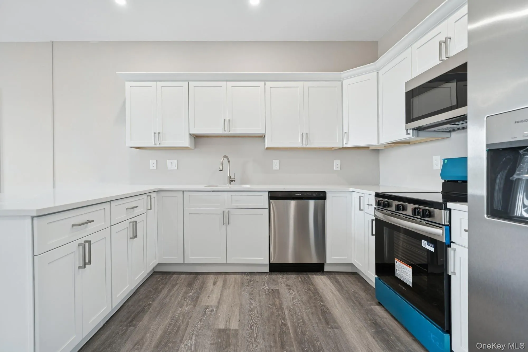 Kitchen featuring stainless steel appliances, wood finished floors, a peninsula, white cabinetry, and light countertops Kitchen featuring stainless steel appliances, wood finished floors, a peninsula, white cabinetry, and light countertops