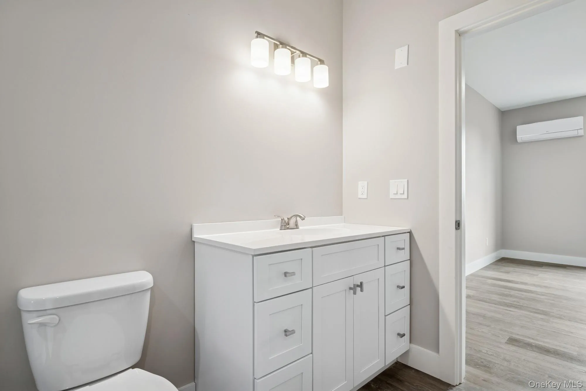 Bathroom with an AC wall unit, vanity, and wood finished floors Bathroom with an AC wall unit, vanity, and wood finished floors