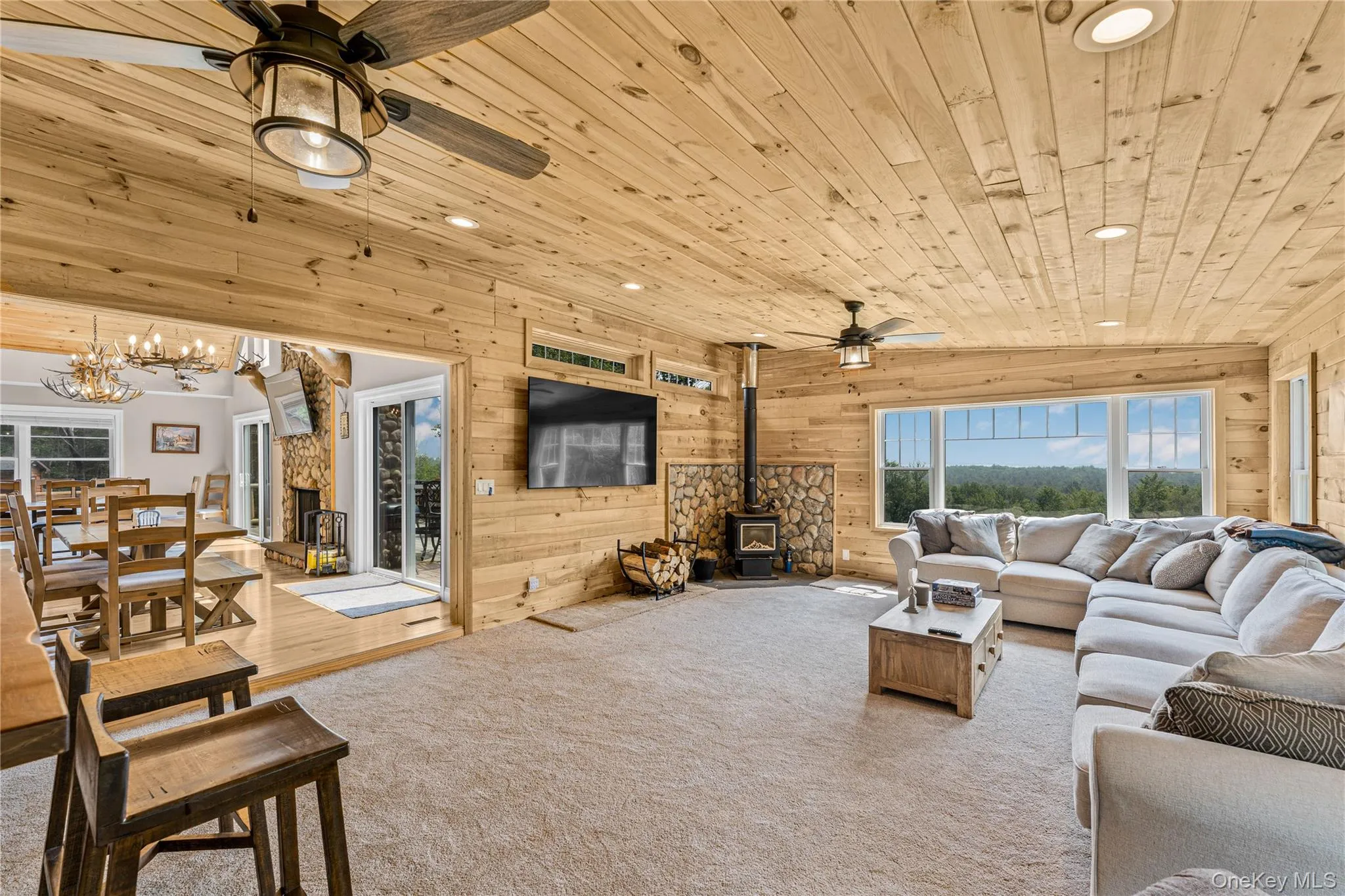 Carpeted living room featuring a wood stove, recessed lighting, wooden walls, ceiling fan, and wood ceiling Carpeted living room featuring a wood stove, recessed lighting, wooden walls, ceiling fan, and wood ceiling